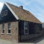 Grotendeels houten woninkje onder zadeldak tussen puntgevels, elk met houten top voorzien van een topmakelaar
